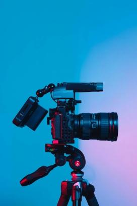 Image contains a large black camera against a blue and purple background