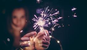 Hands in foreground holding a sparkler with blurred head in background